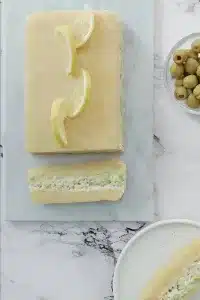Layered vegan causa made with yellow potatoes, cauliflower filling, and avocado, topped with lemon slices on a marble board.