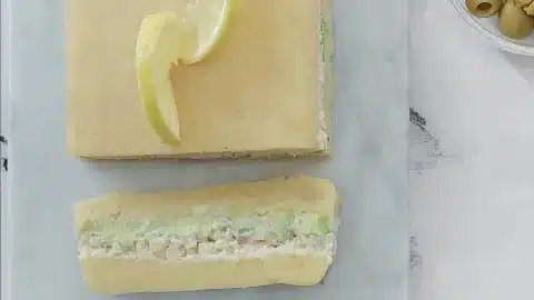Layered vegan causa made with yellow potatoes, cauliflower filling, and avocado, topped with lemon slices on a marble board.