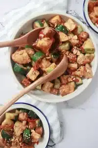 Serving spicy vegan Rojak salad with wooden salad spoons, showing chunks of tofu and vegetables in tamarind-peanut sauce