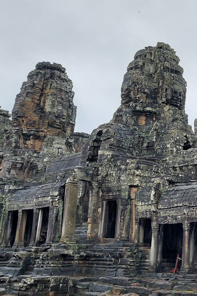 Ancient stone faces of Bayon Temple in Angkor Thom, showcasing intricate Khmer architecture amidst moss-covered ruins.