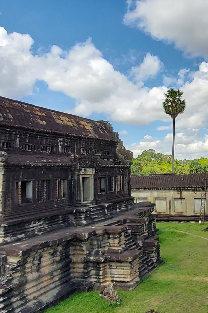 Side view of Angkor Wat temple, showcasing intricate stone carvings and lush greenery under a bright blue sky