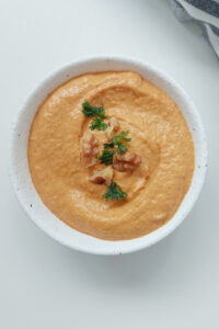 Creamy vegan muhammara dip topped with chopped walnuts and fresh parsley, served in a white bowl.
