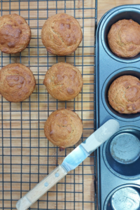 Vegan banana muffins on a wire rack next to a muffin tin and butter knife.