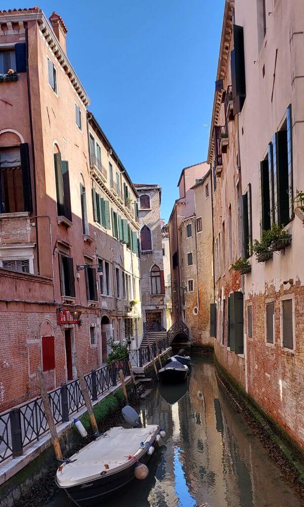 Narrow canal in Venice with boats and pastel-colored buildings. italy itinerary 5 days