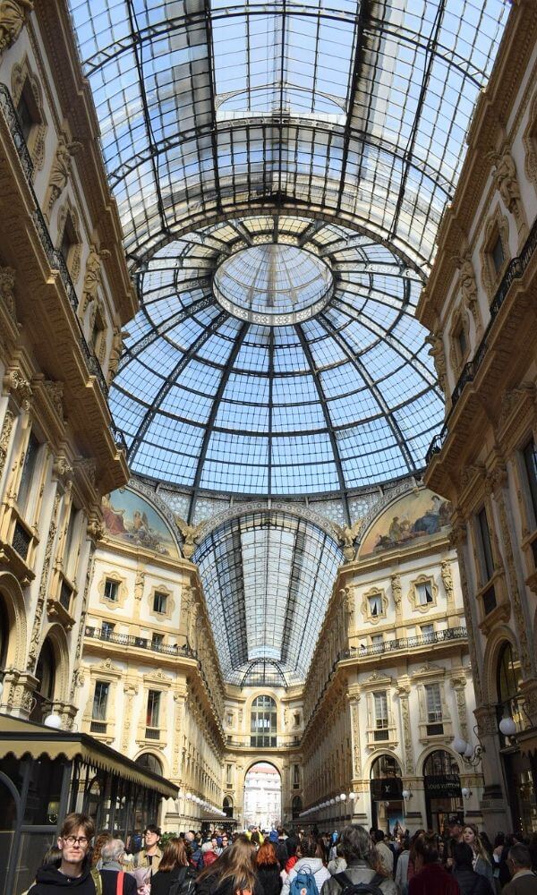 Glass dome and ornate architecture of the Galleria Vittorio Emanuele II filled with people shopping and exploring.