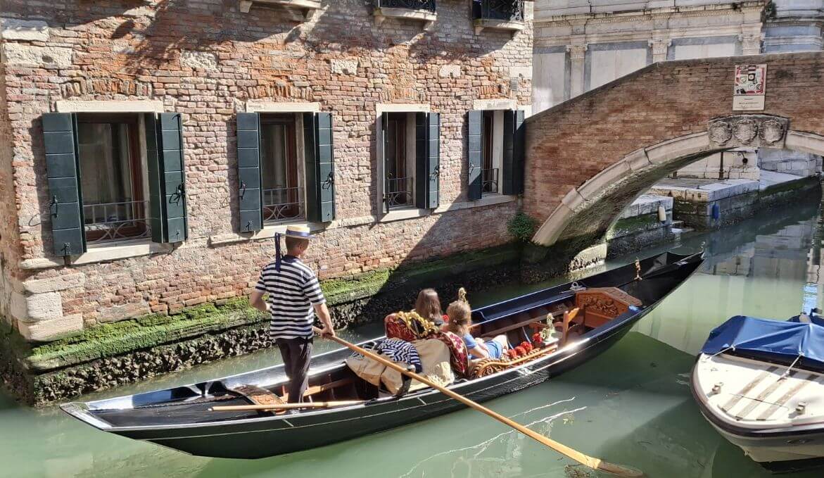Gondolier rowing under a small bridge near brick buildings in a Venice canal. italy itinerary 5 days